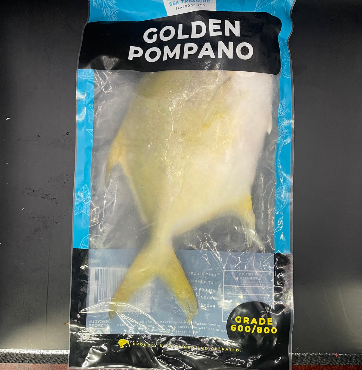 Packaged Golden Pompano fish with a blue and black label on a dark background
