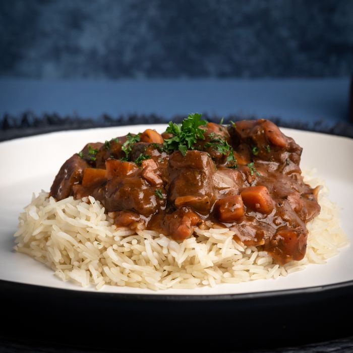 Stew over rice on a white plate with a dark background