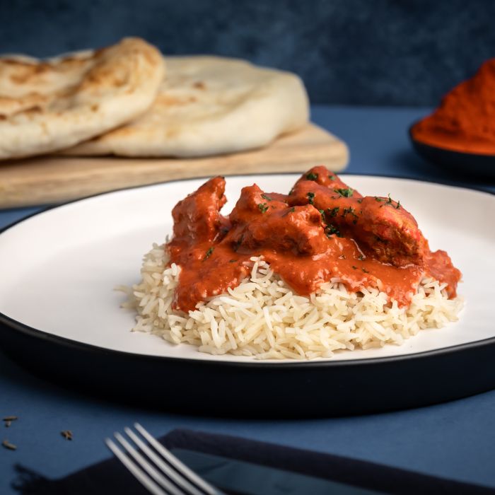 Plated dish of rice with red curry and naan bread on a blue background