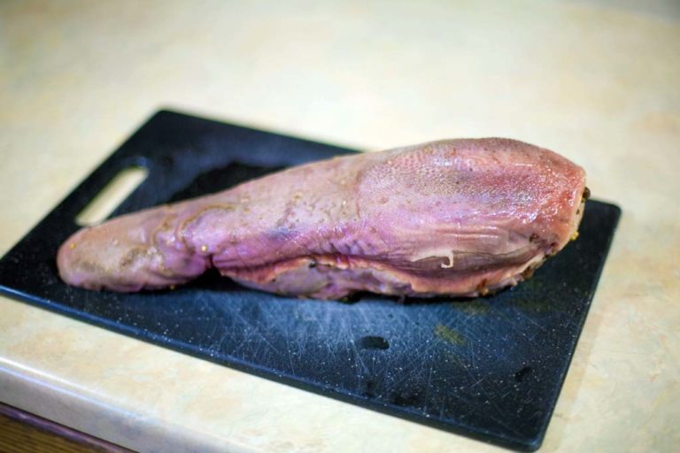 Raw duck leg on a black cutting board with a beige background