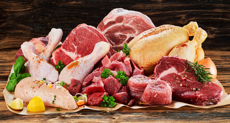Raw meat assortment, beef, chicken, decorated with greens and vegetables, placed on cooking paper on wooden table