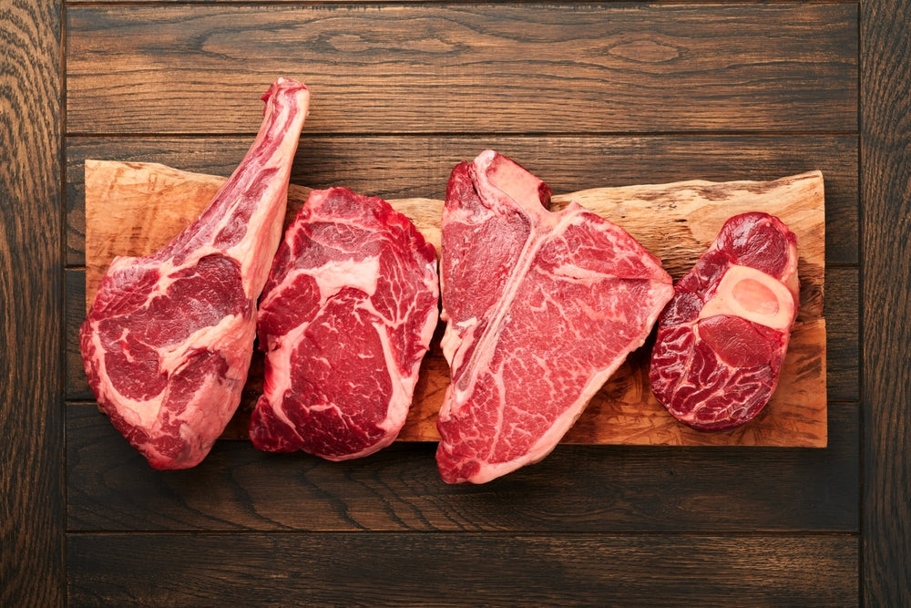 Raw prime steaks. Variety of fresh black angus prime meat steaks T-bone, New York, Ribeye, Striploin, Tomahawk cutting board on black or dark background. Set of various classic steaks. Top view. 