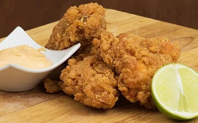 Fried chicken pieces on a wooden board with a side of dipping sauce and a lime wedge.