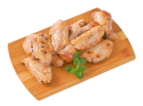 Raw chicken wings on a wooden cutting board with a sprig of rosemary.
